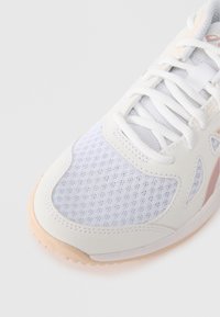 Λευκό αθλητικό παπούτσι με πλέγμα, υφασμάτινα δέρματα και ροζ λογότυπο. Διαθέτει στρογγυλή μύτη, δέσιμο με κορδόνια και μπεζ καουτσούκ σόλα.