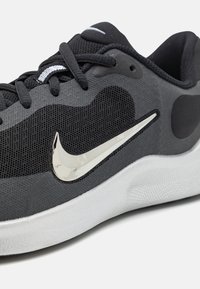 Scarpa sportiva nera con tomaia in rete, baffo Nike argento, colletto imbottito e suola texturizzata. Presenta un design liscio e ammortizzato.