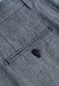 Tissu texturé à rayures bleues marine et blanches, avec une poche poitrine et un bouton noir à quatre trous.