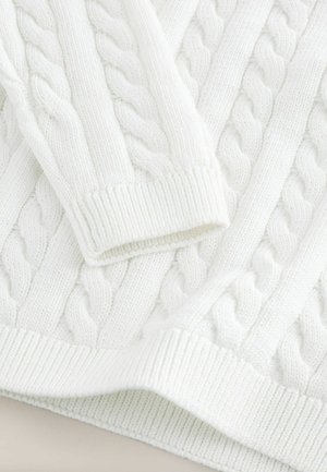 Fehér kötött pulóver, hajtogatott mintázattal. Rugalmas mandzsettákkal és szegéllyel rendelkezik, bemutatva egy texturált, puha anyagot.
