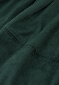 Sötétzöld velúr anyag, amely puha tapintású, látható varratokkal és sima felülettel rendelkezik, drapériákat és redőket mutatva.