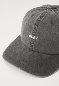 Šedá denimová čiapka so zahnutým štítkom a vyšitým textom "OBEY" v bielej farbe na prednej strane. Obsahuje detaily šitia a štruktúrovanú korunku.