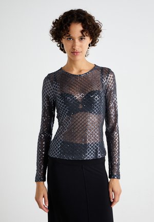 Mesh long-sleeve top in black with a diamond pattern, featuring a sheer design and a round neckline, paired with a black skirt.