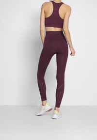 Burgundská sportovní souprava obsahující cropped top s designem racerback a legíny s vysokým pasem a texturovanými akcenty podél nohou.