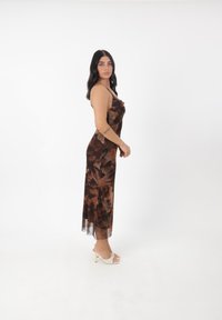 Robe midi à fleurs brune avec des bretelles spaghetti, en tissu transparent, et une silhouette fluide, assortie à des sandales à talons clairs.