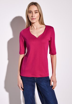 Fuchsia V-Ausschnitt T-Shirt mit kurzen Ärmeln, aus weichem Stoff, mit körperbetontem Schnitt und glatter Textur, kombiniert mit dunklen Jeans.