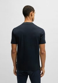 T-shirt a maniche corte di colore blu navy realizzato in un tessuto morbido; presenta un colletto a girocollo con cuciture a contrasto e un orlo dritto con fessure laterali.