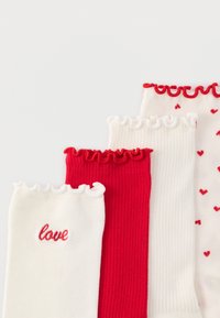 Fyra par vita och röda ribbade strumpor med veckade kanter; en vit strumpa har röd text "love", en annan har ett mönster med små röda hjärtan.
