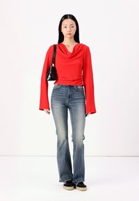 Rød kappe-hals langermet topp, teksturert stoff; blå vide jeans; svart skulderveske; mørke sko med beige såler. Minimalistisk design.