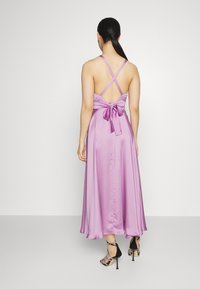Robe en satin violet avec un design à dos croisé, mettant en avant un nœud noué à la taille et une jupe pleine et fluide.