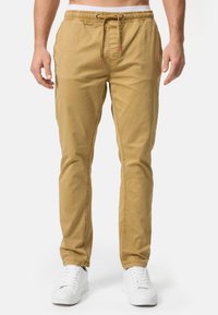 Pantalones jogger de algodón beige con cintura elástica y cordón, que cuentan con bolsillos laterales y una pierna ajustada, combinados con zapatillas blancas.