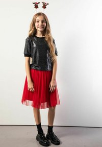 Czarny krótki top z cekinami, czerwona spódnica z tiulu, czarne skarpetki i czarne lakierowane buty; włosy ozdobione porożem renifera.