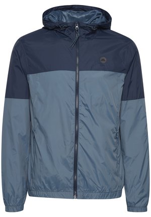 Navy and light blue windbreaker jacket with a hood, featuring a zip front, elastic cuffs, and a logo on the chest. Smooth texture.