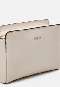 Bolso de piel beige con logo dorado "LIU JO", textura suave, forma rectangular y bordes oscuros en contraste. Cierre superior con cremallera.