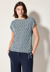 Modrý a bílý krátký rukáv top s potiskem listů, má uvolněný střih a nastavitelnou šňůrku po straně. Kombinováno s námořnickými kalhotami.