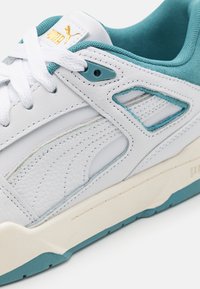 Vita lädersneakers med turkosa detaljer, texturerad häl och perforerad sidopanel. Har vita snörningar och en beige gummisula.