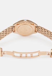 Złoty różowy metalowy zegarek z teksturowanym, połączonym paskiem. Obejmuje okrągłą kopertę, błyszczący koronkę oraz grawerowane detale z tyłu.