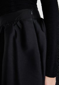 Saia preta com um acabamento suave em satin e textura franzida na cintura, com um fecho de correr escondido na lateral.