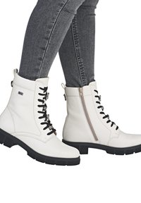 Stivali alla caviglia in pelle bianca con lacci neri, cerniera laterale e suola in gomma nera testurizzata. I leggeri dettagli di cucitura accentuano il design.