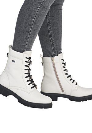 Bottines en cuir blanc avec lacets noirs, fermeture éclair sur le côté et semelle en caoutchouc noir texturée. Des surpiqûres légères accentuent le design.