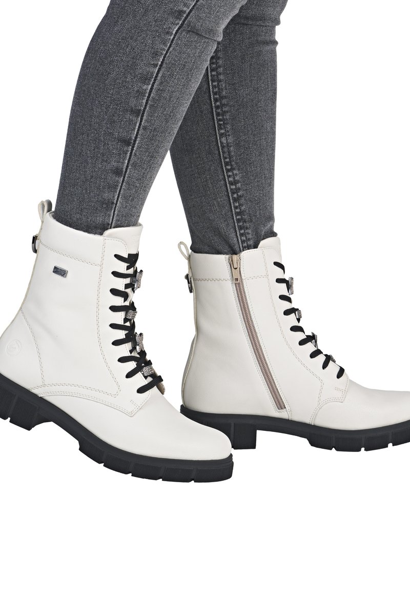 Stivali alla caviglia in pelle bianca con lacci neri, cerniera laterale e suola in gomma nera testurizzata. I leggeri dettagli di cucitura accentuano il design.