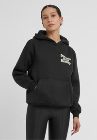 Zwarte hoodie met een voorzak en een capuchon met koord. De tekst "Dreams Over Reality" is in crème kleur op de borst gedrukt.
