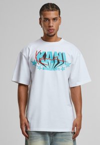 White short-sleeve T-shirt featuring bold turquoise and red graphic text with stars. Loose fit, made of soft cotton fabric.