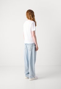 Balti trumpa rankovė t-shirt, laisvas fasonas, derinama su šviesiai mėlynais laisvais džinsais ir baltais sportbačiais, rodomas iš nugaros. Lygi tekstūra, kasdienis dizainas.