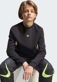 Black sweatshirt with green Adidas logo, round neck, and raglan sleeves. Paired with black pants featuring green Nike accents.