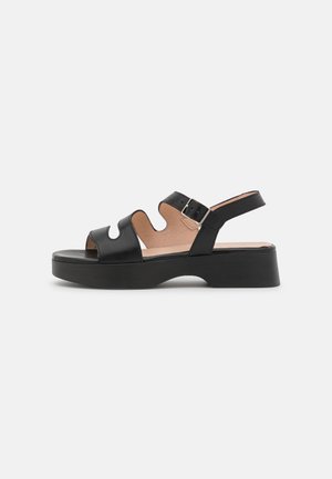 Black leather open-toe sandal with wave cutouts, buckle strap, and low chunky heel on a white background.