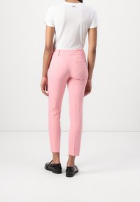 Pantalons rose clair au design ajusté, fabriqués en tissu lisse, avec une taille mi-haute et des poches arrière discrètes. Des chaussures noires complètent le look.