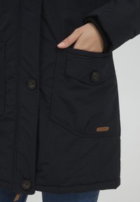 Marineblauwe geïsoleerde jas met een knoopsluiting aan de voorkant, zijzakken met knoopsluiting en een leren logo label op de onderzak.