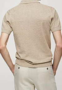 Polo shirt beige en maille avec des manches courtes, un col replié et un ourlet côtelé, associé à un pantalon de couleur claire avec des accents métalliques.
