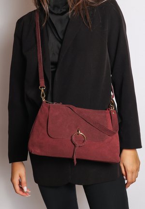 Borsa a tracolla in suede bordeaux con hardware dorato, chiusura a pattina, dettaglio circolare e tracolla regolabile. Finitura testurizzata e linee pulite.