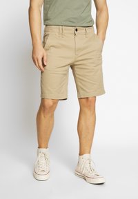 Beiga bomullsshorts med rak skärning, utrustade med bälteshällor och framfickor. Bärs med vita högklackade sneakers.
