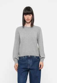 Suéter gris de punto con escote redondo, mangas largas y un corte relajado, combinado con jeans de mezclilla azules. Textura suave, diseño minimalista.