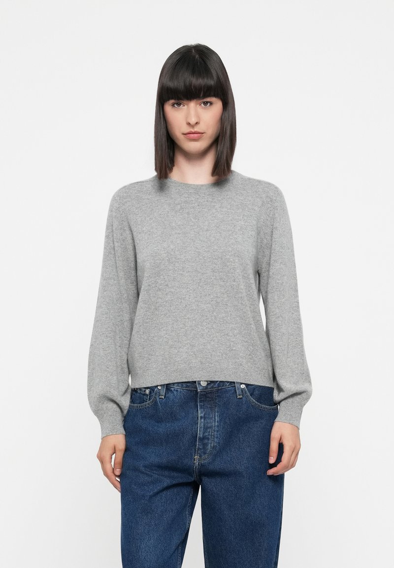 Suéter gris de punto con escote redondo, mangas largas y un corte relajado, combinado con jeans de mezclilla azules. Textura suave, diseño minimalista.