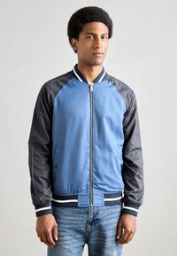 Blaue und schwarze Bomberjacke mit Reißverschluss vorne, weißem gestreiftem Kragen und strukturiertem Stoff. Verfügt über seitliche Taschen und gerippte Bündchen.