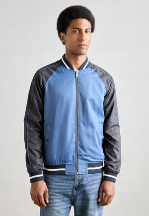 Blaue und schwarze Bomberjacke mit Reißverschluss vorne, weißem gestreiftem Kragen und strukturiertem Stoff. Verfügt über seitliche Taschen und gerippte Bündchen.
