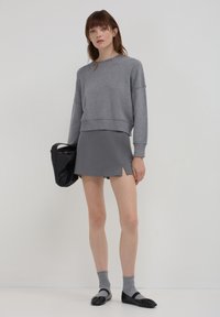 Pull gris court avec ourlet côtelé, mini jupe grise assortie avec fentes sur les côtés, chaussettes grises et ballerines noires. Sac à main noir inclus.