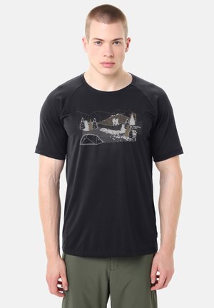 Uomo che indossa una maglietta nera con grafica di montagna e foresta per escursionismo e pantaloni verdi, in piedi su uno sfondo chiaro uniforme.