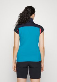 Kortärmad atletisk topp i teal med marineblå och rosa accenter. Slät textil, ståkrage, figursydd design, tillsammans med svarta shorts.