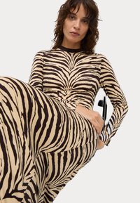 Długo rękawowa, dopasowana sukienka z miękkiego materiału, z beżową bazą i czarnymi paskami w zebra oraz okrągłym dekoltem.