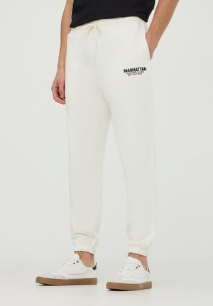 Białe dresy z regulowanym pasem, ściągaczami na końcach nogawek oraz czarnym napisem "MANHATTAN" na lewym udzie. Wykonane z miękkiego materiału będącego mieszanką bawełny.