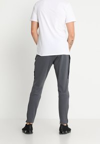 Harmaat juoksuhousut mustilla sivupaneeleilla, kapeat malli, joustava vyötärö ja sileä kangas. Yhdistetty yksinkertaiseen valkoiseen t-paitaan.