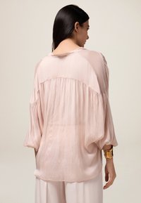 Lange mouwen, lichtroze blouse met een losse pasvorm, voorzien van gerimpelde details bij de schouders en een zachte, doorschijnende textuur.