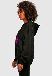 Felpa nera con zip, con una grande grafica viola, tasca a marsupio frontale, vestibilità rilassata, polsini a costine e texture morbida.