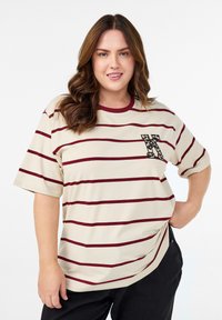 Beige striped t-shirt features maroon horizontal lines, a crew neckline, and a leopard-patterned pocket accent. Fabric appears soft and relaxed.