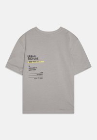 Camiseta de algodón gris con texto impreso en negro y amarillo. El diseño incluye detalles de temática urbana y un ajuste relajado. Mangas cortas.