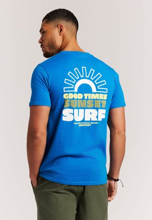 Blauw katoenen T-shirt met een groot wit en geel grafisch ontwerp op de achterkant, met de tekst "GOOD TIMES SUNSET SURF" en zonnestralen erboven.
